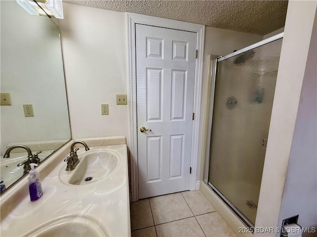 bathroom with double vanity, a stall shower, a sink, a textured ceiling, and tile patterned flooring