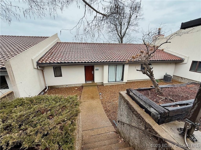 view of front facade featuring a tile roof, cooling unit, and stucco siding