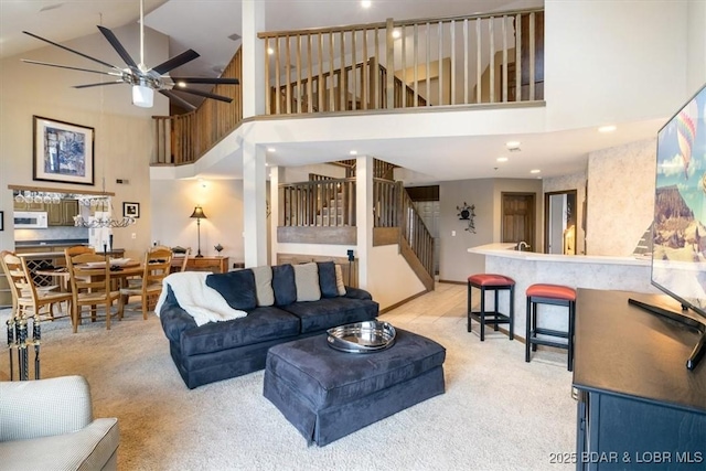 living area with light carpet, ceiling fan, a high ceiling, and stairway