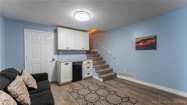 living area with visible vents, stairway, light wood-style floors, a textured ceiling, and baseboards