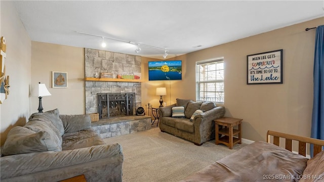 carpeted living room featuring a stone fireplace and rail lighting