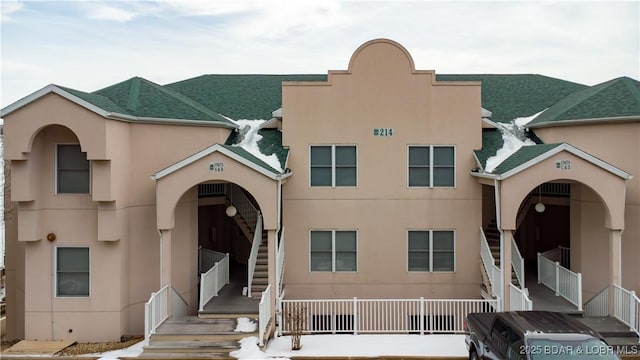 view of front facade featuring a shingled roof, stairway, and stucco siding