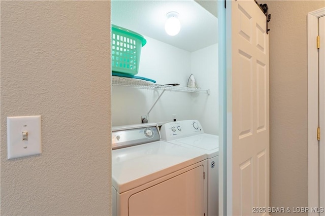 laundry area with laundry area, a barn door, washer and clothes dryer, and a textured wall