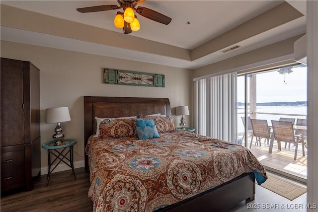 bedroom with a tray ceiling, visible vents, wood finished floors, access to outside, and baseboards