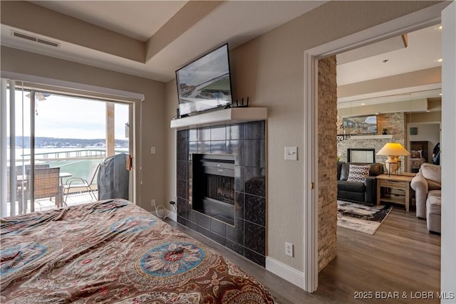 bedroom with access to outside, visible vents, wood finished floors, a tile fireplace, and baseboards