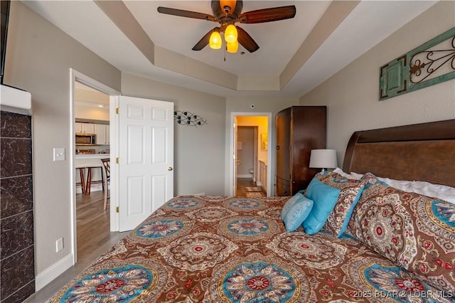 bedroom featuring ensuite bathroom, a tray ceiling, a ceiling fan, and baseboards