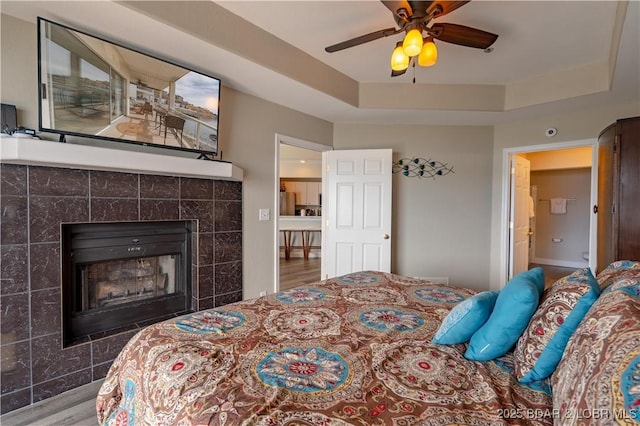 bedroom featuring a fireplace, a ceiling fan, a raised ceiling, and wood finished floors