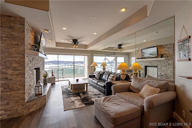 living area featuring ceiling fan, recessed lighting, a large fireplace, dark wood-style flooring, and a raised ceiling