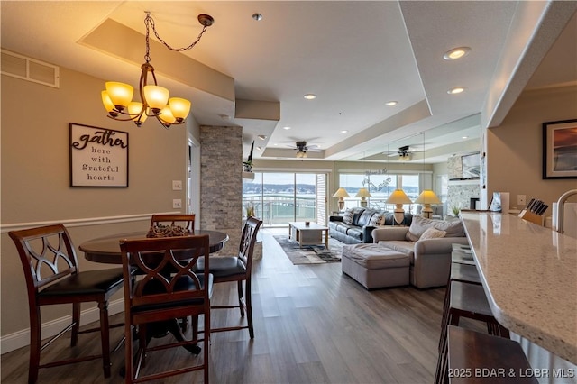 dining room featuring visible vents, a tray ceiling, wood finished floors, and ceiling fan with notable chandelier