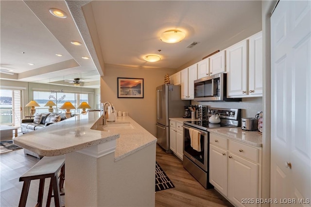 kitchen with a breakfast bar area, a sink, visible vents, white cabinetry, and appliances with stainless steel finishes