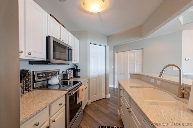 kitchen with light stone counters, dark wood-style flooring, stainless steel appliances, white cabinetry, and a sink