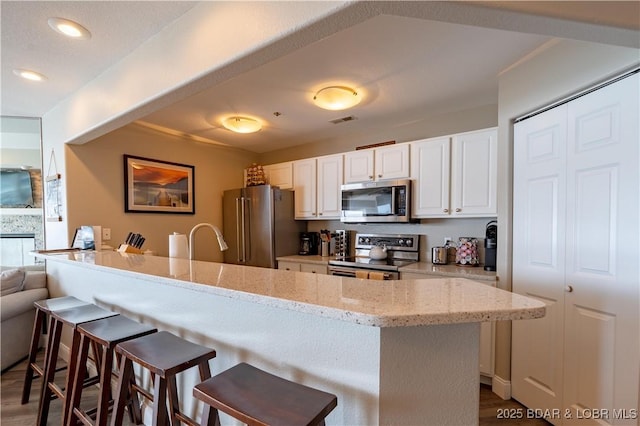 kitchen with white cabinetry, visible vents, a kitchen breakfast bar, appliances with stainless steel finishes, and light stone countertops