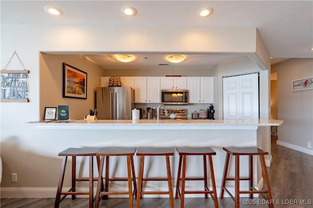 kitchen featuring white cabinets, appliances with stainless steel finishes, a breakfast bar, and dark wood finished floors