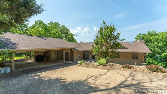 ranch-style home with a shingled roof, an attached carport, driveway, and a chimney