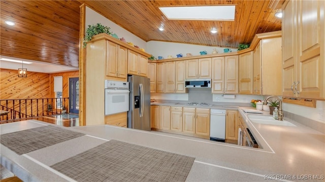 kitchen featuring vaulted ceiling with skylight, stainless steel appliances, a sink, wood ceiling, and light brown cabinetry