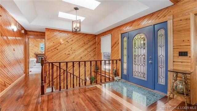 entryway featuring wood walls, a skylight, wood finished floors, baseboards, and a tray ceiling