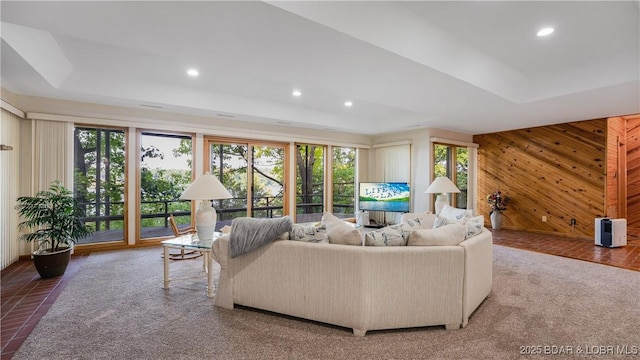 living room featuring a tray ceiling, wooden walls, and recessed lighting