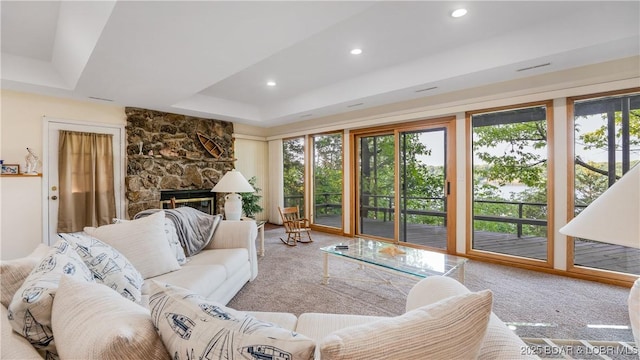 carpeted living room featuring a stone fireplace, a raised ceiling, and recessed lighting