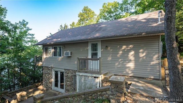 rear view of house with a wall unit AC, stone siding, roof with shingles, and french doors