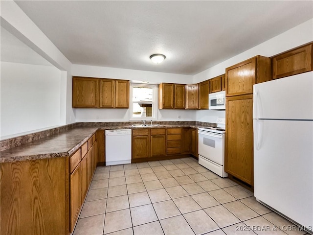 kitchen with a peninsula, white appliances, a sink, brown cabinetry, and dark countertops