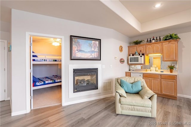 living area with light wood finished floors, baseboards, visible vents, a glass covered fireplace, and recessed lighting