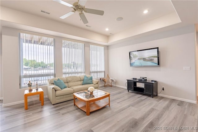 living room featuring a tray ceiling, light wood-type flooring, visible vents, and baseboards