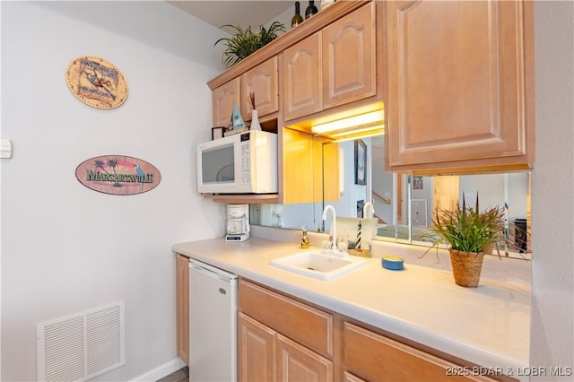 kitchen with white appliances, light brown cabinets, visible vents, and a sink