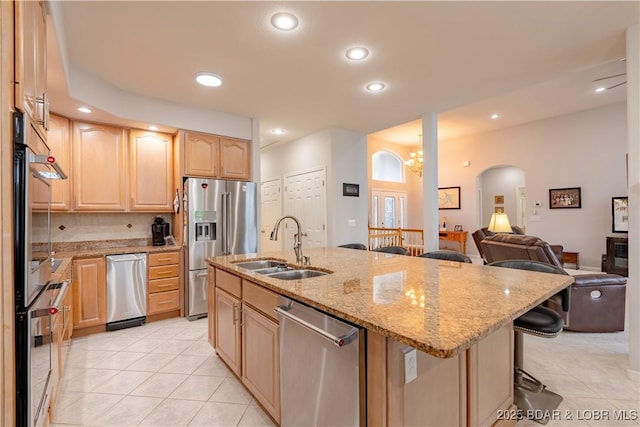 kitchen featuring appliances with stainless steel finishes, open floor plan, a breakfast bar, light brown cabinetry, and a sink