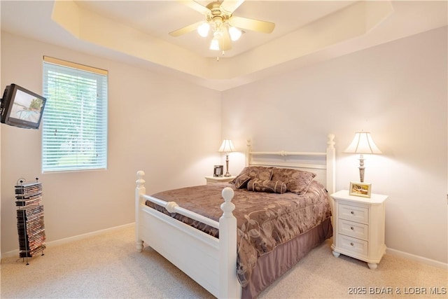 bedroom with a ceiling fan, a tray ceiling, light colored carpet, and baseboards