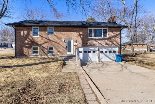 split foyer home featuring brick siding, driveway, a chimney, and a garage