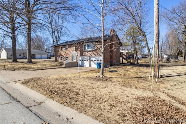 view of front facade with stairway, brick siding, concrete driveway, and a chimney