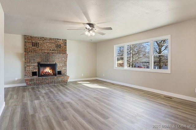 unfurnished living room featuring visible vents, a fireplace, baseboards, and wood finished floors