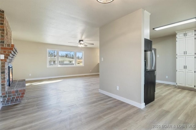 unfurnished living room with a ceiling fan, a fireplace, light wood-style floors, and baseboards