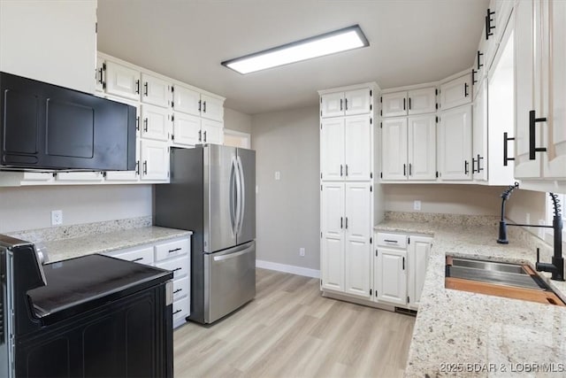 kitchen featuring black range with electric stovetop, freestanding refrigerator, light wood-style floors, white cabinetry, and a sink