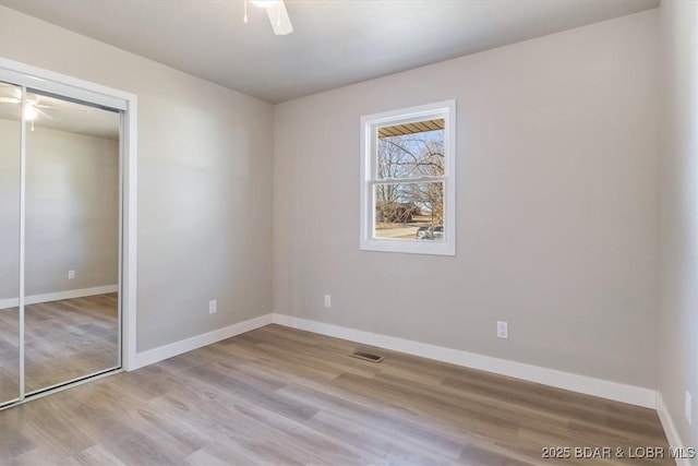 unfurnished bedroom featuring wood finished floors, visible vents, baseboards, ceiling fan, and a closet