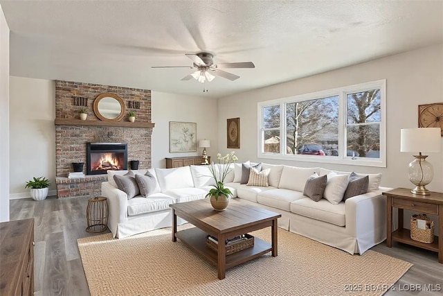 living area with ceiling fan, a textured ceiling, wood finished floors, and a fireplace