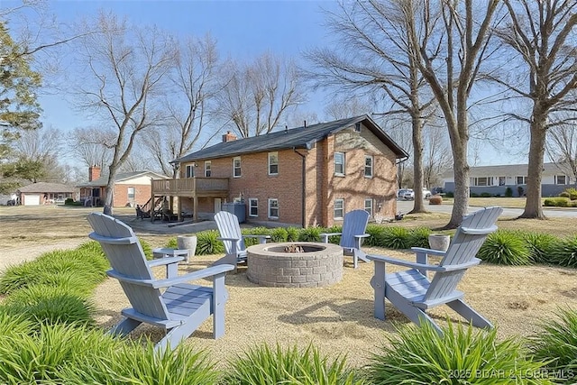 rear view of property featuring cooling unit, a wooden deck, stairs, a fire pit, and brick siding