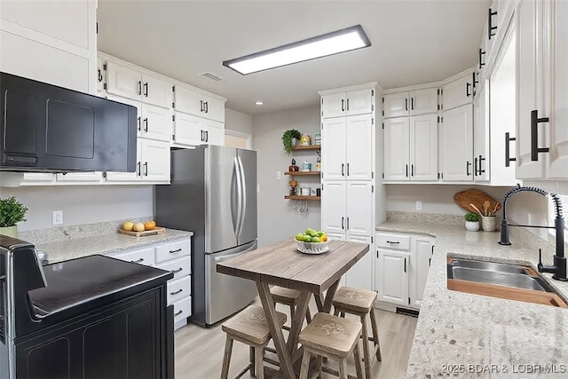 kitchen with white cabinetry, freestanding refrigerator, and a sink