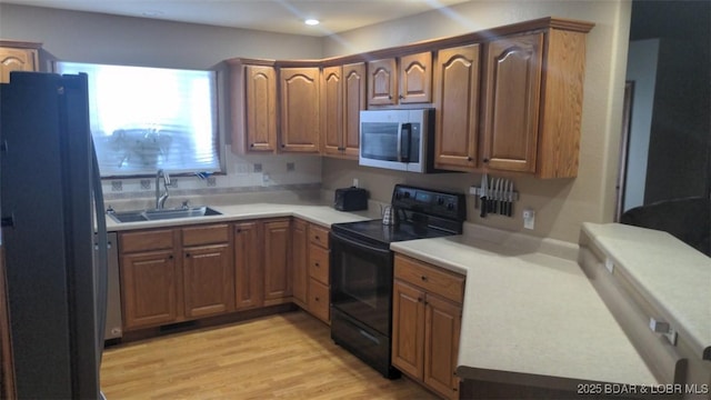 kitchen with stainless steel microwave, light wood-style floors, freestanding refrigerator, a sink, and black range with electric cooktop