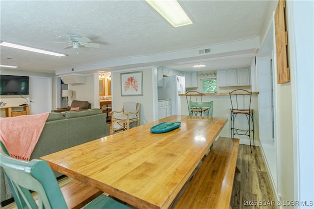 dining room featuring a ceiling fan, visible vents, a textured ceiling, and wood finished floors