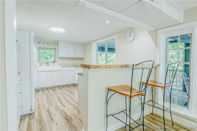 kitchen featuring freestanding refrigerator, white cabinetry, a sink, light wood-type flooring, and a kitchen breakfast bar