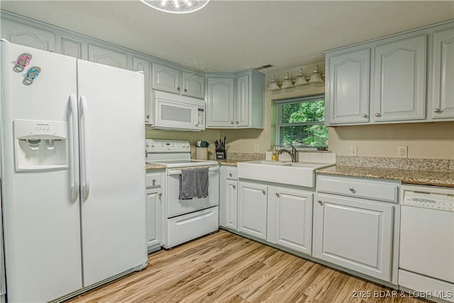 kitchen with white appliances, light wood finished floors, and a sink