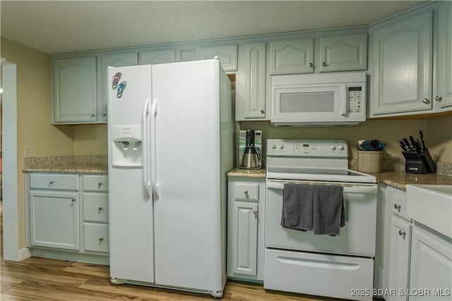 kitchen featuring white appliances, light stone counters, and light wood-style floors