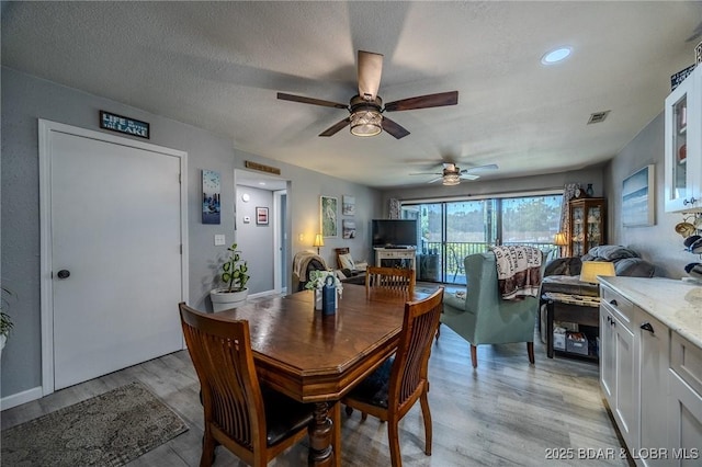 dining space featuring light wood-style floors, visible vents, and a textured ceiling