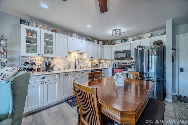 kitchen with stainless steel appliances, light countertops, glass insert cabinets, white cabinetry, and a sink