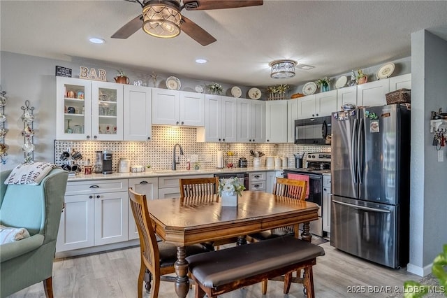 kitchen with light countertops, appliances with stainless steel finishes, light wood-style floors, white cabinets, and a sink