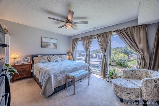 bedroom with a textured ceiling, visible vents, a ceiling fan, and light colored carpet