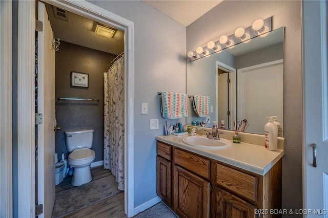 bathroom featuring visible vents, toilet, vanity, wood finished floors, and baseboards