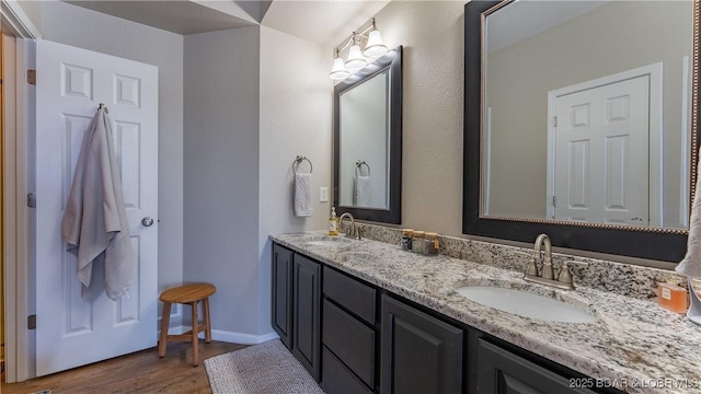 full bath featuring double vanity, baseboards, a sink, and wood finished floors