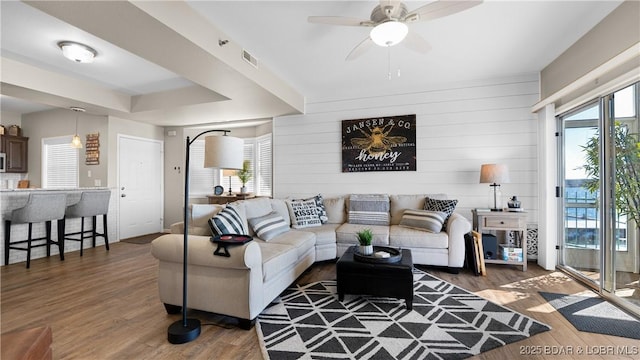 living room with a raised ceiling, wood finished floors, visible vents, and a ceiling fan